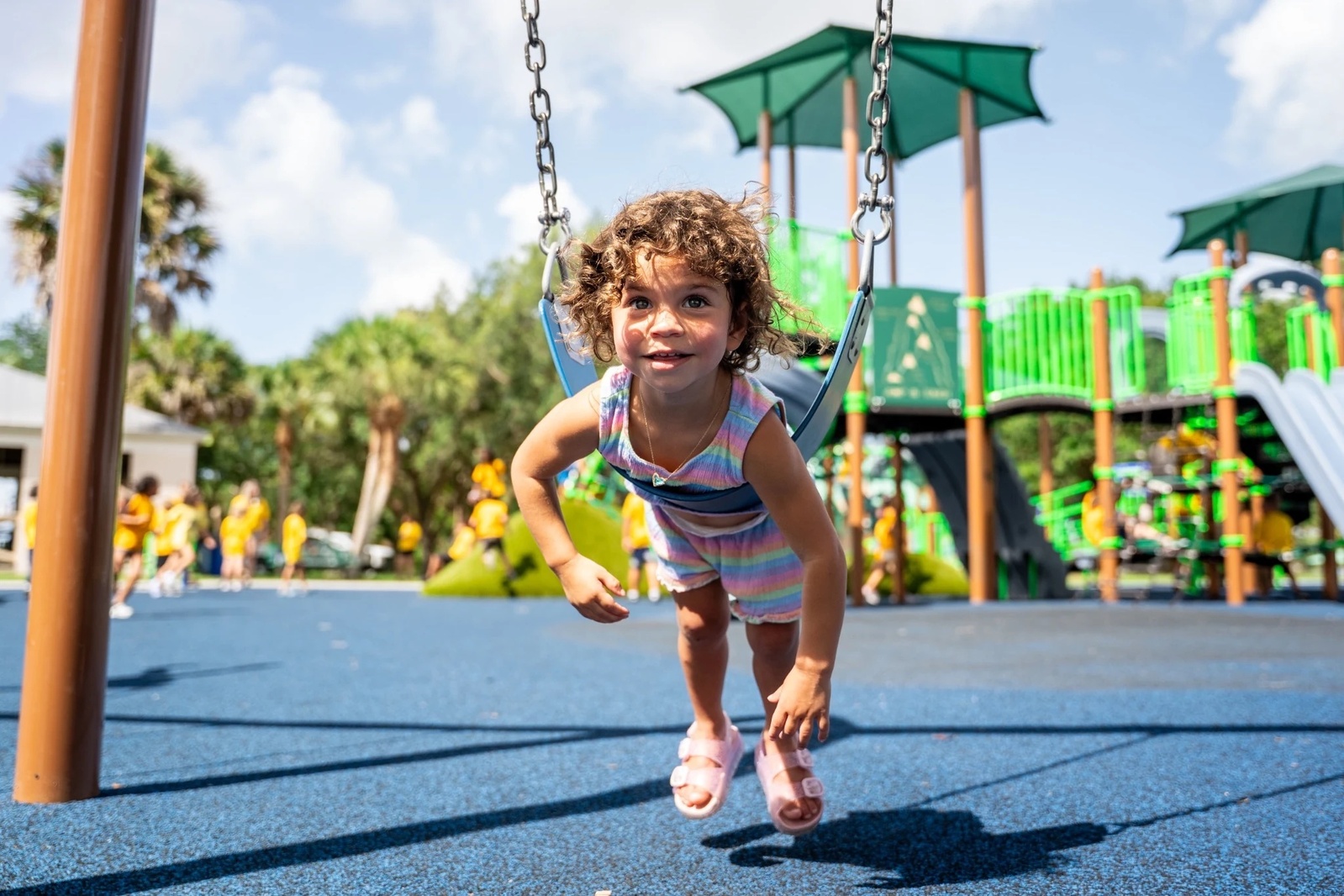A child laughing on a swing, with green roofs and climbing equipment behind