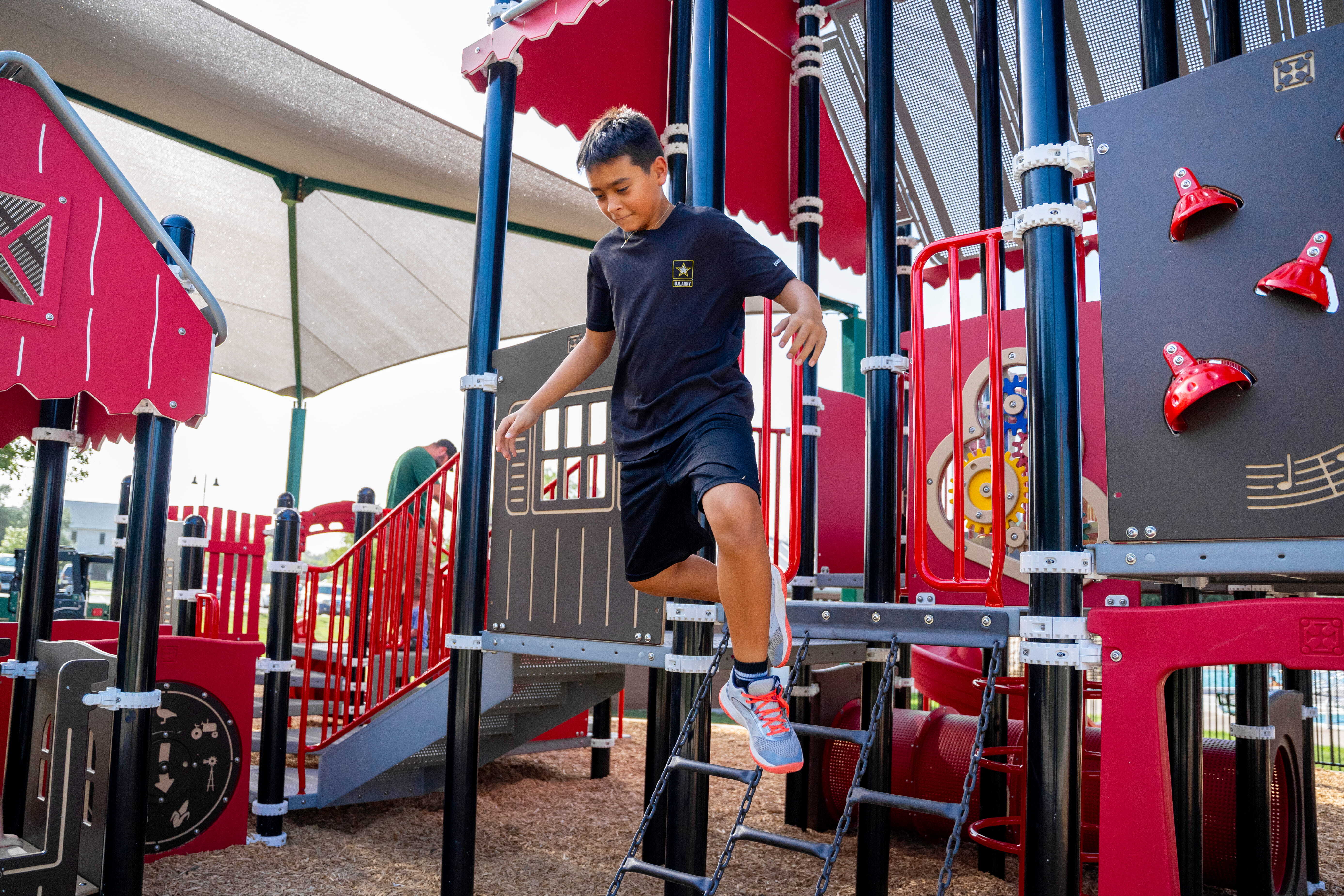 Child climbing a ladder on the red and black playground structure at Heritage Park in Texas.